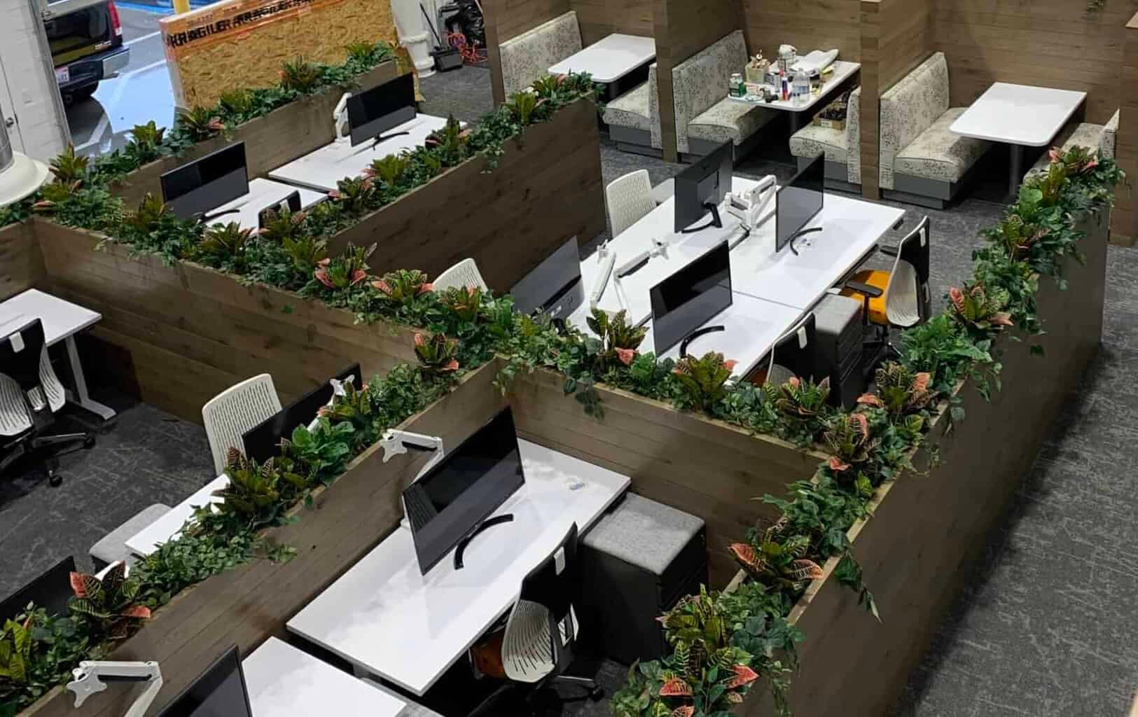 Contemporary office with artificial greenery, dividers and white desks for a productive environment.